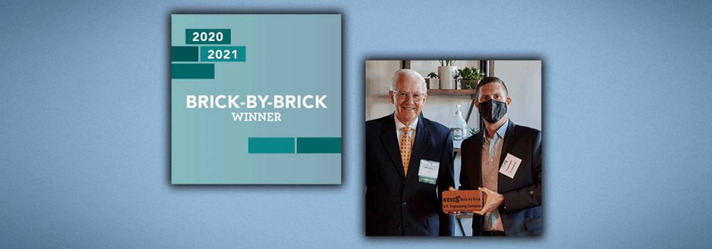 A graphic with 2020 2021 BRICK-BY-BRICK WINNER next to a photo of two men in suits, one holding a brick-shaped award and the other smiling; one man is wearing a face mask.