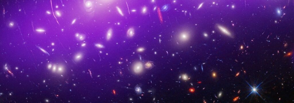 An image of deep space shows numerous galaxies and bright stars scattered across a dark background with a purple glow at the top. The scene highlights a vast, colorful cosmic landscape.