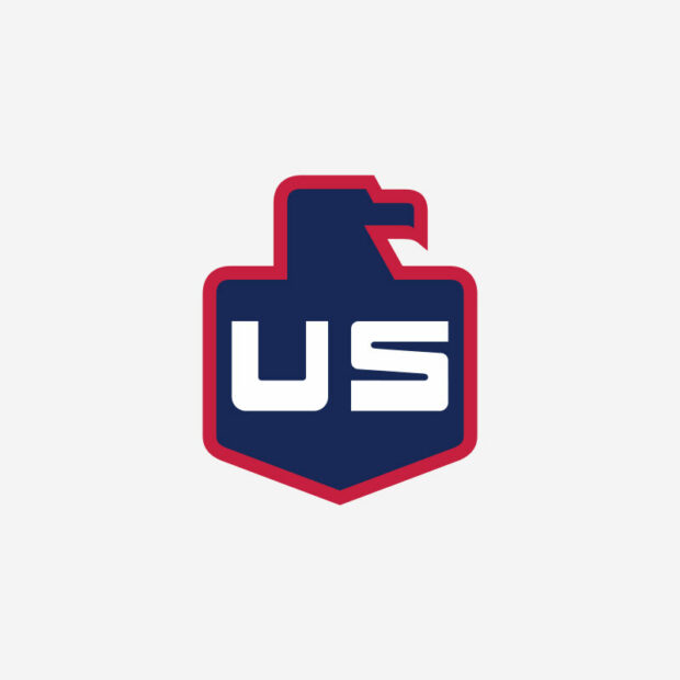 A navy blue shield-shaped logo with US in bold white letters. The top of the shield forms a stylized eagle head facing right. The outline of the shield is red. The background is light gray.