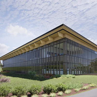 A modern two-story building with large glass windows and a flat, overhanging roof, surrounded by landscaped greenery under a partly cloudy sky.